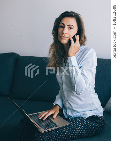 Woman working on laptop calling on phone at home Woman working on laptop calling on phone at home 108212089