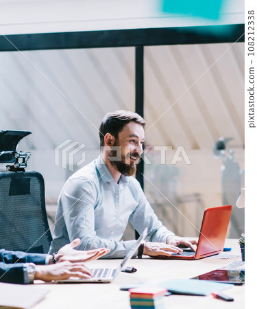 Cheerful colleagues interacting in office with laptops 108212338