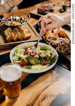Close up of male hands eating fresh tasty salad in restaurant during dinner with friends 108212982