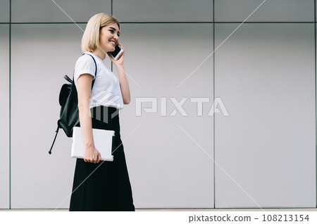 Smiling adult modern female talking on mobile strolling on street 108213154