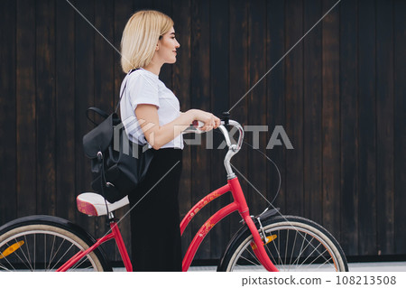Adult female cyclist walking with bicycle on street Adult female cyclist walking with bicycle on street 108213508