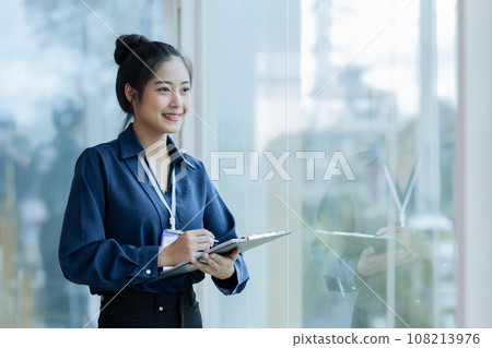 Businesswoman working on digital tablet while standing in front of windows Businesswoman working on digital tablet while standing in front of windows 108213976