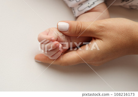 Parents' hands hold the fingers of a newborn baby. The hand of a mother and father close-up holds the fist of a newborn baby. Family health and medical care. Professional photo on white background Parents' hands hold the fingers of a newborn baby. The hand of a mother and father close-up holds the fist of a newborn baby. Family health and medical care. Professional photo on white background 108216173