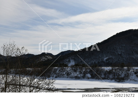 A view of the river flowing from Shichikashuku Dam, which is covered with snow in front of the snowy mountain. 108219272