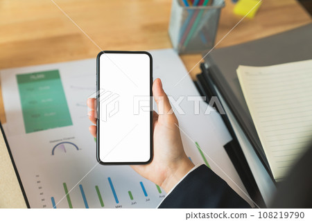 Businessman hand holding black smartphone with blank screen on desk in the office. 108219790