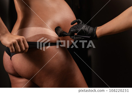 The master evens out an instant tan with a brush on the skin of a pregnant woman. Close-up of the tummy. The master evens out an instant tan with a brush on the skin of a pregnant woman. Close-up of the tummy. 108220231
