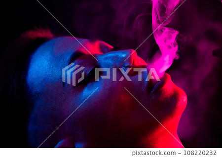 Portrait asian woman with shaved temples smokes vape in neon light. Portrait asian woman with shaved temples smokes vape in neon light. 108220232