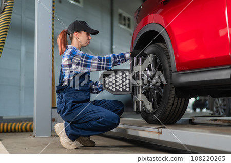 A female auto mechanic makes a camber. Woman working in a car service. 108220265