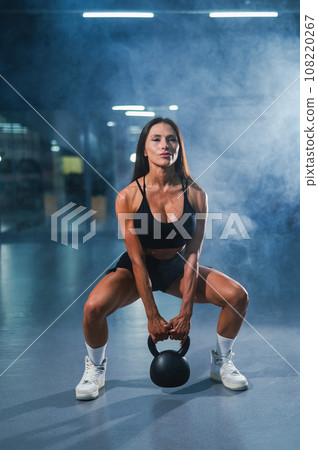 Caucasian woman squats with a kettlebell in the gym. Vertical photo. 108220267