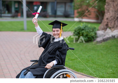 Happy caucasian woman in a wheelchair holding her diploma outdoors. 108220385
