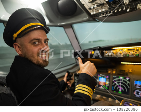 Caucasian bearded man smiling while driving a flight simulator. Pilot in the cockpit showing thumbs up. Caucasian bearded man smiling while driving a flight simulator. Pilot in the cockpit showing thumbs up. 108220386