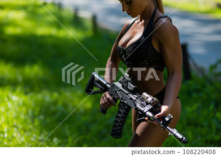 Caucasian woman in bikini with machine gun outdoors. Caucasian woman in bikini with machine gun outdoors. 108220408