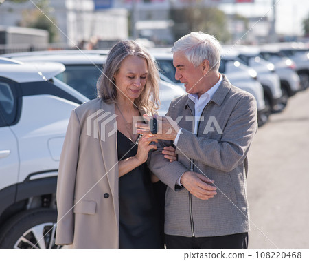 Mature Caucasian couple standing by a car outdoors. Elderly man holding car keys.  108220468