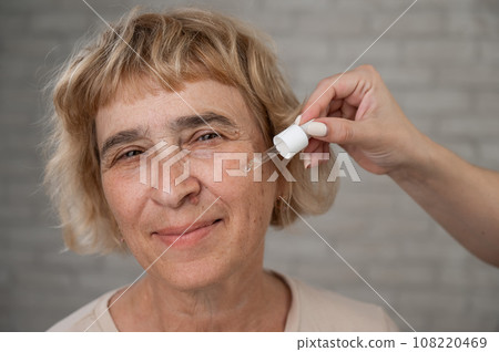 Close-up portrait of an old woman applying hyaluronic acid serum with a pipette. Anti-aging face care.  108220469