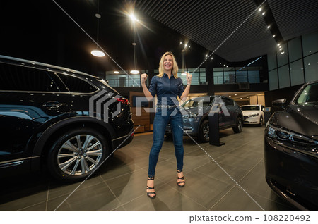 Young caucasian woman rejoices buying a car in a car dealership.  108220492
