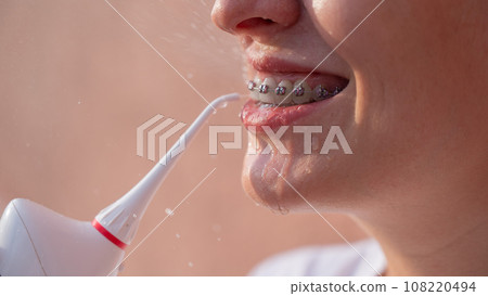 A woman with braces on her teeth uses an irrigator. Close-up portrait.  108220494