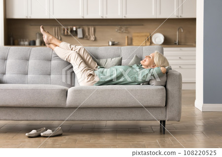 Cheerful sleepy blonde older lady lying on couch Cheerful sleepy blonde older lady lying on couch 108220525