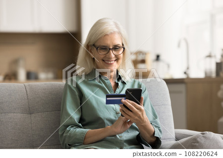 Positive elderly retired woman using online bank application on smartphone Positive elderly retired woman using online bank application on smartphone 108220624