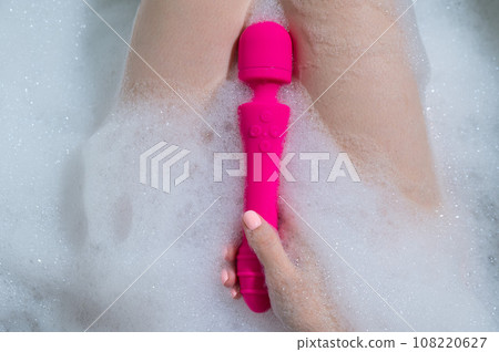 Woman lies in a bubble bath and uses a vibrator. Woman lies in a bubble bath and uses a vibrator. 108220627