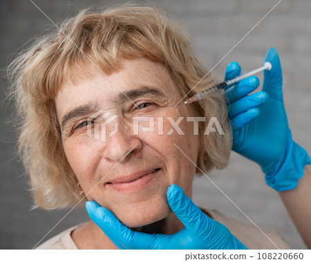 The doctor makes beauty injections in the face of an old caucasian woman. Wrinkles around the eyes.  108220660