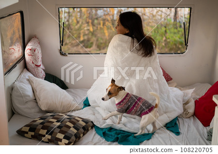 Caucasian woman looks out of the window of the van while hugging her dog Jack Russell Terrier. Travel in a camper in autumn. 108220705