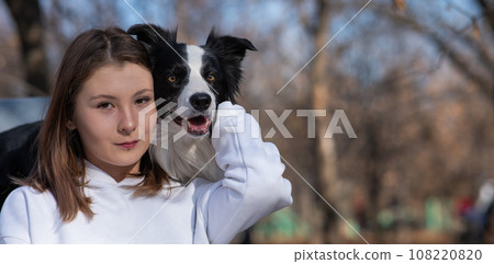 Caucasian woman hugging her dog Border Collie while sitting on a bench in autumn park. 108220820