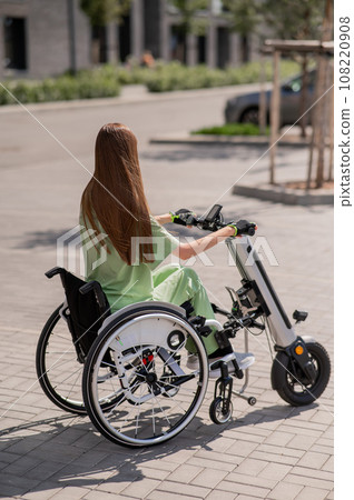 A woman in a wheelchair with an assistive device for manual control. Electric handbike. A woman in a wheelchair with an assistive device for manual control. Electric handbike. 108220908