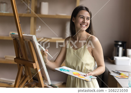 Happy woman holding paintbrush enjoy painting class in creative workshop Happy woman holding paintbrush enjoy painting class in creative workshop 108221030