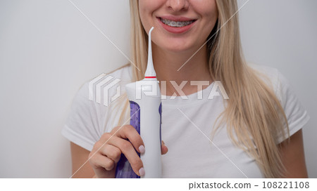 Cropped portrait of a caucasian woman with braces on her teeth holding an irrigator.  108221108