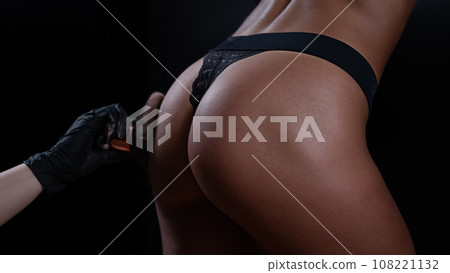 The master uses a brush to apply matting powder to the woman's buttocks after the instant tanning procedure. The master uses a brush to apply matting powder to the woman's buttocks after the instant tanning procedure. 108221132
