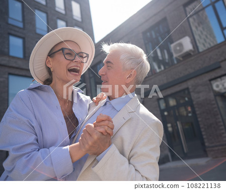 An elderly couple in love dances outdoors. A gray-haired man and a mature woman laugh and hug. An elderly couple in love dances outdoors. A gray-haired man and a mature woman laugh and hug. 108221138