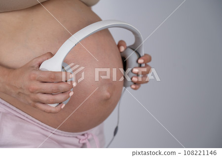 A pregnant woman holds headphones against her bare tummy. The expectant mother lets her child listen to music.  108221146