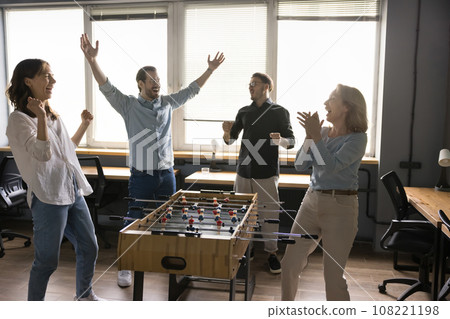 Cheerful euphoric colleagues playing table soccer at lunch break Cheerful euphoric colleagues playing table soccer at lunch break 108221198