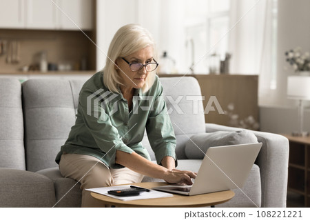 Serious blonde elderly woman in glasses doing domestic financial work Serious blonde elderly woman in glasses doing domestic financial work 108221221