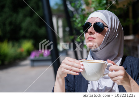 Caucasian woman in hijab drinking coffee in outdoor cafe. Caucasian woman in hijab drinking coffee in outdoor cafe. 108221222