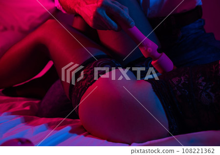 A man and a woman in a bedroom in red blue neon light use a dildo. Faceless couple in sexual games. 108221362