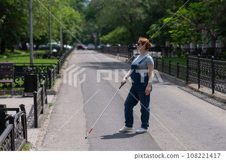 Blind pregnant woman crosses the street with the help of a tactile cane. 108221417