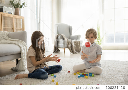 Brother and sister play with toys on floor at home 108221418