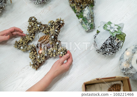 A woman makes Christmas decorations in the form of a star from cones. Top view of the process of making souvenirs 108221466