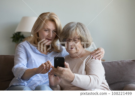 Middle aged caregiver woman teaching old lady to use smartphone Middle aged caregiver woman teaching old lady to use smartphone 108221499