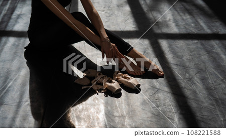 Faceless ballerina sits on the floor and puts on pointe shoes. Faceless ballerina sits on the floor and puts on pointe shoes. 108221588