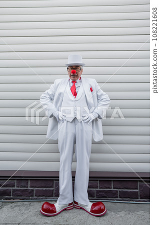 Full-length portrait of a clown in a white classic suit and a vintage tall hat. Full-length portrait of a clown in a white classic suit and a vintage tall hat. 108221608