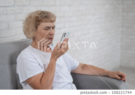 An elderly Caucasian woman suffers from myopia and tries to read a message on a smartphone. An elderly Caucasian woman suffers from myopia and tries to read a message on a smartphone. 108221744