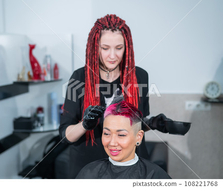 The hairdresser dyes the hair of an Asian woman in pink. Short extreme haircut. The hairdresser dyes the hair of an Asian woman in pink. Short extreme haircut. 108221768