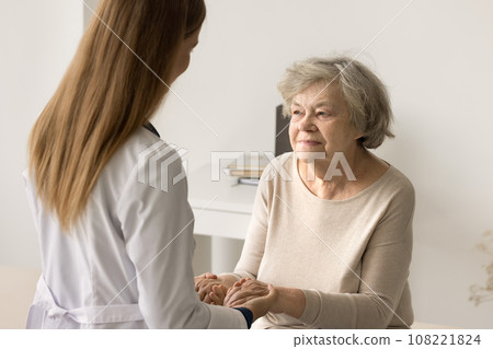 Caring young therapist in white uniform holding hands of patient 108221824