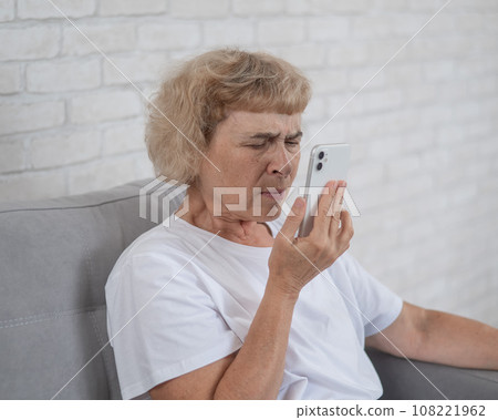 An elderly Caucasian woman suffers from myopia and tries to read a message on a smartphone. An elderly Caucasian woman suffers from myopia and tries to read a message on a smartphone. 108221962