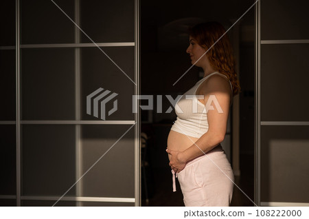 A pregnant woman in shorts and a crop top stands in profile between folding doors. A pregnant woman in shorts and a crop top stands in profile between folding doors. 108222000