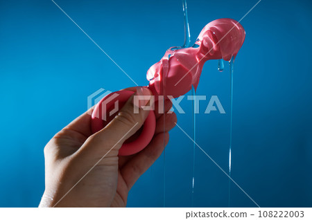 Woman pouring lubricant on pink anal beads on blue background. Woman pouring lubricant on pink anal beads on blue background. 108222003