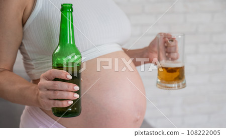 Pregnant woman holding glass and bottle of beer.  108222005