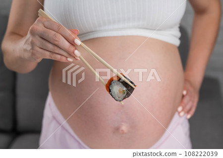 A pregnant woman holds a roll with chopsticks. Close-up of the belly. A pregnant woman holds a roll with chopsticks. Close-up of the belly. 108222039